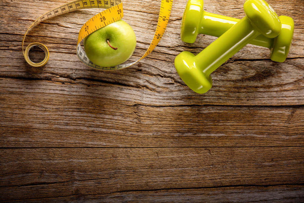 Weight loss secrets from the National Weight Control Registry - Two dumbbells,green apple, measuring tape on wooden background